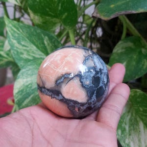 May include: A polished sphere of pink and gray stone with a swirling pattern. The sphere is smooth and has a high gloss finish.