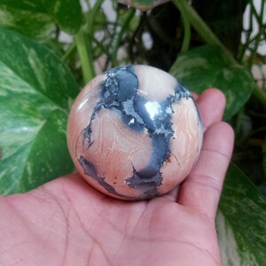 May include: A smooth, polished sphere of pink and gray agate with a swirling pattern. The sphere is about the size of a golf ball.