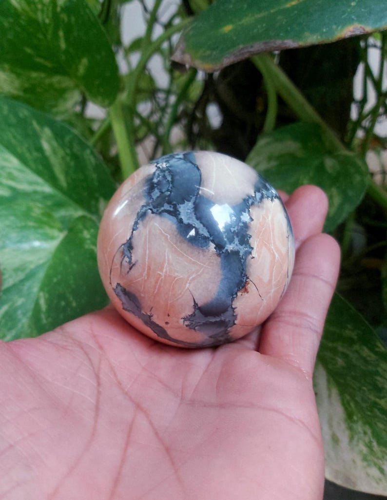 May include: A smooth, polished sphere of pink and gray agate with a swirling pattern. The sphere is about the size of a golf ball.