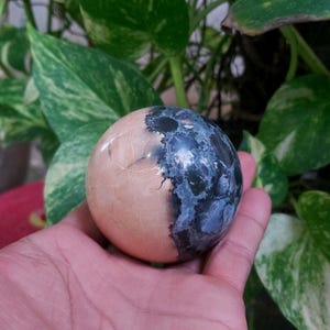 May include: A smooth, round, polished stone sphere with a half-and-half design. One half is a light pink color, and the other half is a dark blue with white speckles.