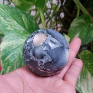 May include: A dark gray and white sphere with a light brown center. The sphere is made of a natural stone and has a smooth, polished surface.