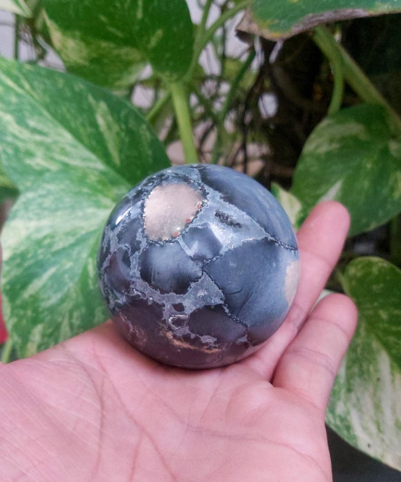May include: A dark gray and white sphere with a light brown center. The sphere is made of a natural stone and has a smooth, polished surface.