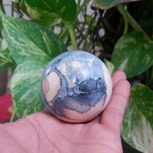 May include: A smooth, round, blue and white agate sphere with swirling patterns. The sphere is about the size of a golf ball.