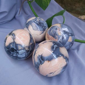 May include: Four smooth, round, polished spheres of pink and gray stone. The spheres have a mottled, marbled pattern.