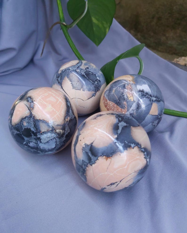May include: Four smooth, round, polished spheres of pink and gray stone. The spheres have a mottled, marbled pattern.
