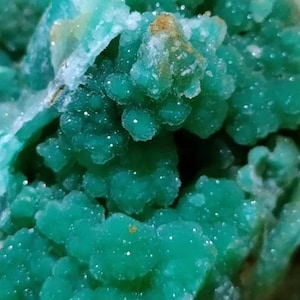 May include: Close-up of a green, crystalline mineral with a rough, textured surface. The mineral has a bright, vibrant green color and appears to be made up of many small, individual crystals.