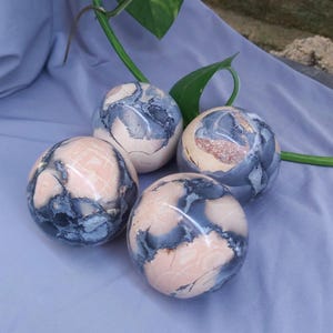 May include: Four pink and gray patterned spheres made of polished stone. The spheres are arranged in a semi-circle on a light blue surface.