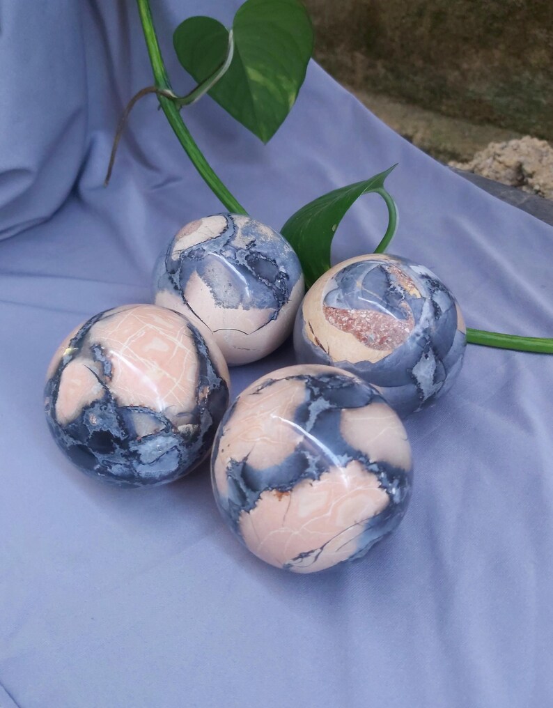 May include: Four pink and gray patterned spheres made of polished stone. The spheres are arranged in a semi-circle on a light blue surface.