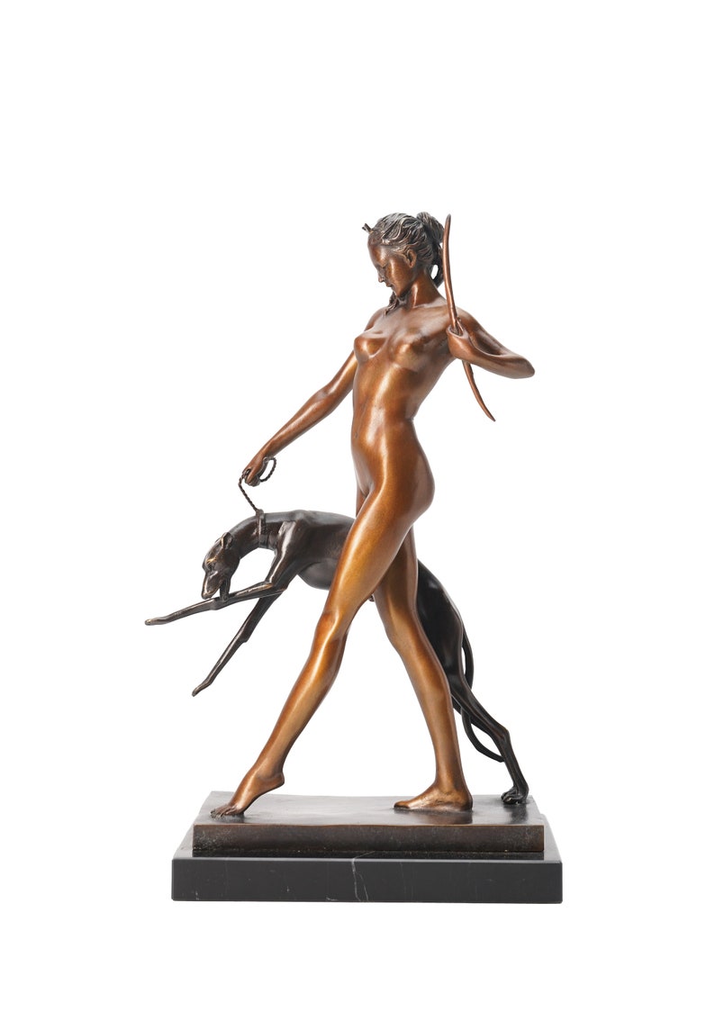 May include: A bronze sculpture of a standing figure holding a bow and a leash attached to a dark-toned greyhound. The figure is depicted in a walking pose, mounted on a rectangular black marble base with a smooth, polished metallic finish.
