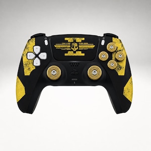 May include: A black video game controller featuring yellow distressed patterns, a central yellow skull emblem, and gold-coloured bullet casing caps on the analogue sticks and action buttons. The directional pad is white, and the controller has a matte finish.