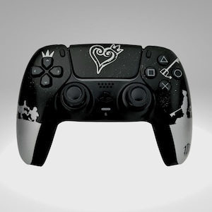 Peut inclure: Une manette PlayStation 5 DualSense noire avec un design personnalisé représentant un logo et des personnages Kingdom Hearts argentés. La manette est noire et argentée et a une surface texturée.
