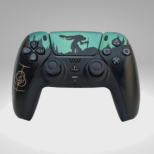 May include: A black PlayStation 5 DualSense controller with a custom design featuring a silhouette of a figure with a sword against a teal and green background. The controller has gold accents on the left side.