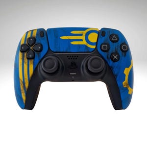 May include: A custom black and blue games controller with yellow detailing. The controller has a blue base with yellow stripes and a yellow gear design. The buttons are black, and it features a PlayStation logo.
