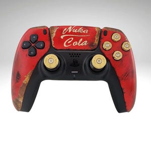 Peut inclure: Une manette de jeu PlayStation 5 rouge et noire avec un design Nuka Cola. La manette a un aspect usé et rouillé et présente des boutons dorés en forme de balle.