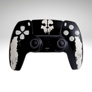 May include: A black PlayStation 5 DualSense controller with a white Ghost of Tsushima skull design on the top. The controller has a white, textured design on the sides.