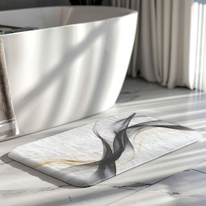 May include: A white bath mat with a black and gold abstract design. The mat is made of a soft, absorbent material and is perfect for adding a touch of style to your bathroom.
