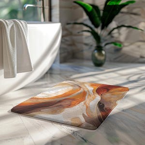 May include: A rectangular bath mat with an abstract design in shades of brown, orange, and cream. The mat is placed on a tiled floor in a bathroom setting, with a white bathtub and a green plant visible in the background.