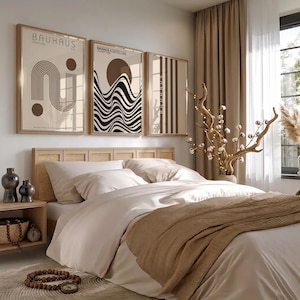 May include: Three framed wall art prints featuring Bauhaus-inspired geometric designs in black, white, and beige. The prints display abstract lines, circles, and wave patterns. The artwork is displayed above a bed with a light wood and cane headboard.