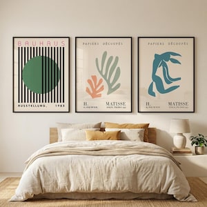May include: Three framed wall art prints displayed above a bed. The left print features a green circle with black vertical lines and the text BAUHAUS AUSSTELLUNG 1923. The two right prints show abstract organic shapes with the text PAPIERS DÉCOUPÉS H. MATISSE.