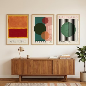 Può includere: Tre stampe d'arte incorniciate disposte in fila. La stampa a sinistra presenta blocchi di colore arancione e rosso con il testo MARK ROTHKO. Quella centrale mostra cerchi sovrapposti in verde e arancione con il testo BAUHAUS 1923 BERLIN. Quella a destra mostra un cerchio verde su strisce verticali nere con il testo BAUHAUS AUSSTELLUNG 1923.