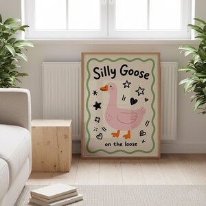 Puede incluir: Un póster enmarcado con una ilustración de un ganso rosa. El texto "Silly Goose" está en la parte superior, con "on the loose" en la parte inferior. La obra de arte está rodeada de estrellas, corazones y otros elementos decorativos.