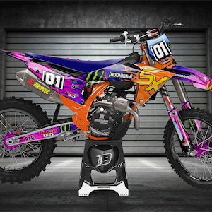 May include: A bright orange, purple, and blue motocross bike with a Monster Energy logo and the number "01" on the side. The bike is on a black stand with white accents.