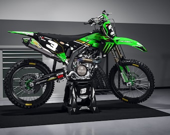 Puede incluir: Una moto de motocross negra y verde con el número 3 en el lateral, sentada en un soporte negro en un garaje.