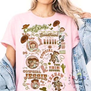 Op de afbeelding: Roze t-shirt met een grafisch ontwerp met een cowgirl-thema. Het ontwerp bevat de tekst "Cowgirl Duty", "Sweetheart of the Rodeo" en "Cowgirl Jessie". Illustraties van een cowgirl, paarden en cowboylaarzen zijn ook aanwezig.