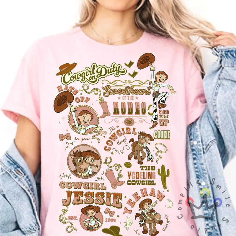 Op de afbeelding: Roze t-shirt met een grafisch ontwerp met een cowgirl-thema. Het ontwerp bevat de tekst "Cowgirl Duty", "Sweetheart of the Rodeo" en "Cowgirl Jessie". Illustraties van een cowgirl, paarden en cowboylaarzen zijn ook aanwezig.
