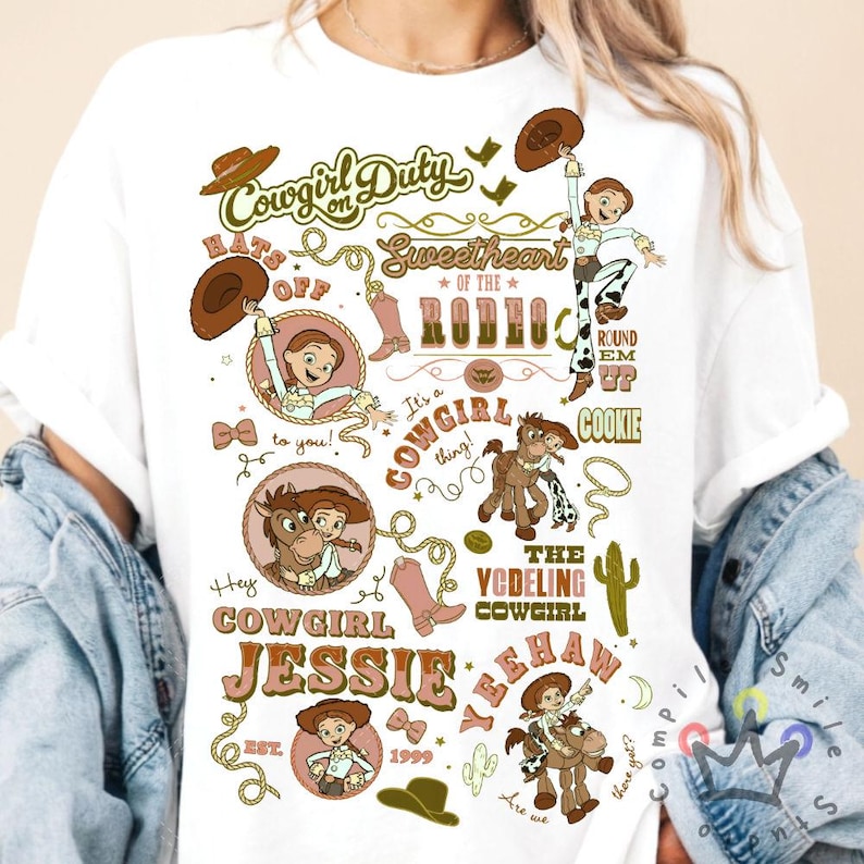 Op de afbeelding: Wit T-shirt met een kleurrijk grafisch ontwerp met de tekst "Cowgirl Jessie" en verschillende illustraties van een cowgirl, een paard en cowboylaarzen. Het ontwerp bevat de tekst "Cowgirl on Duty" en "Sweetheart of the Rodeo".