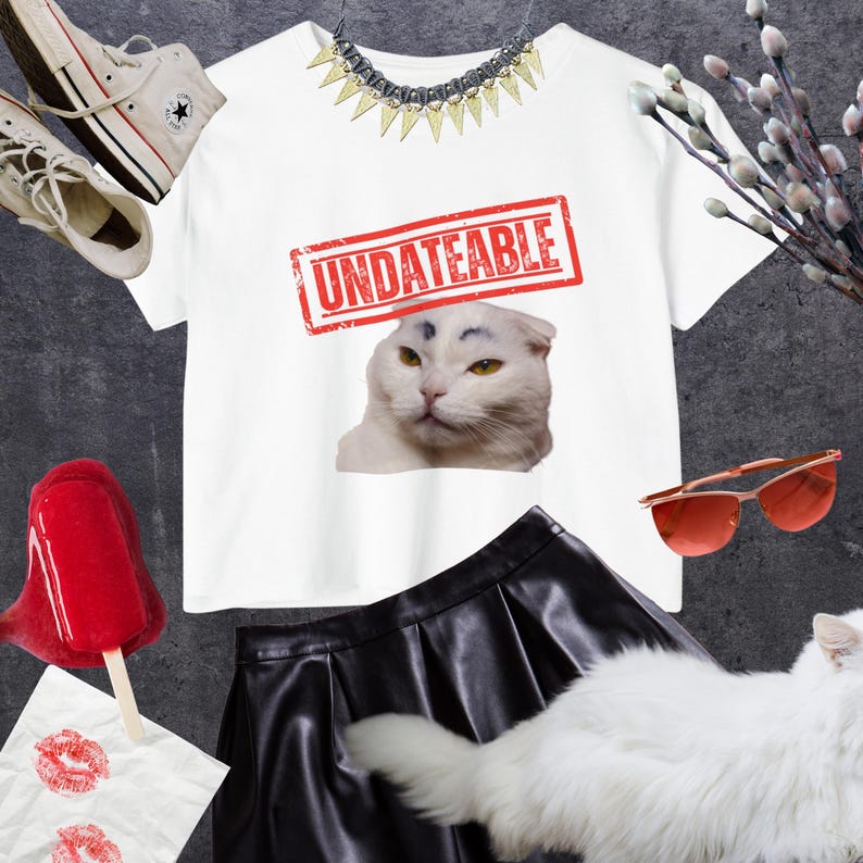 May include: White t-shirt with a red stamp that says "UNDATEABLE" over a cat's face. The image includes a black skirt, red sunglasses, a necklace, and a pair of white sneakers.