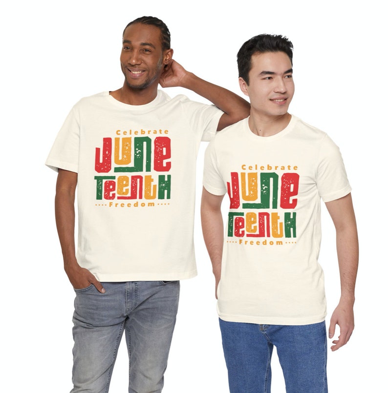 Puede incluir: Dos personas con camisetas blancas con el texto "Celebrate Juneteenth...Freedom..." impreso en rojo, amarillo y verde. Las camisetas son de estilo vintage con un aspecto desgastado.