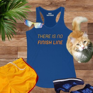 May include: A royal blue tank top with the text "THERE IS NO FINISH LINE" in orange. The tank top is on a wooden surface with a pair of sunglasses, a pair of orange athletic shorts, and a cat.