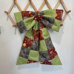 May include: A large decorative bow constructed from a patchwork of fabrics featuring lime green solid panels, grey fabric with circular star patterns, and a dark red print with various Halloween-themed illustrations including pumpkins and witches.
