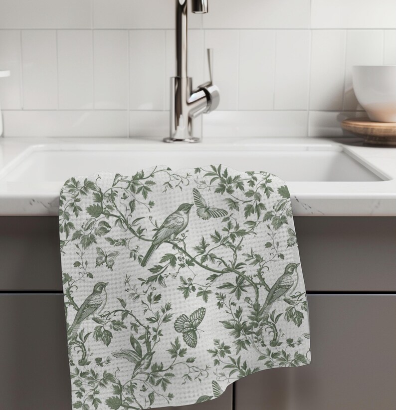 May include: A white kitchen towel with a green floral pattern featuring birds and butterflies. The towel is hanging on a kitchen sink.