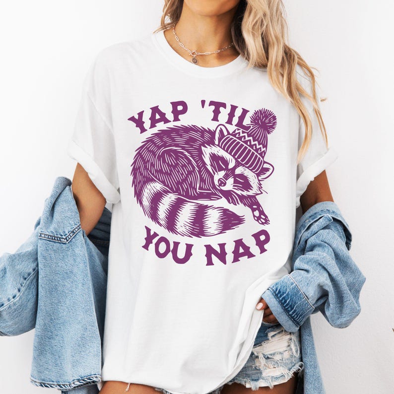 May include: White t-shirt with a purple graphic of a raccoon wearing a hat and the text "YAP 'TIL YOU NAP".
