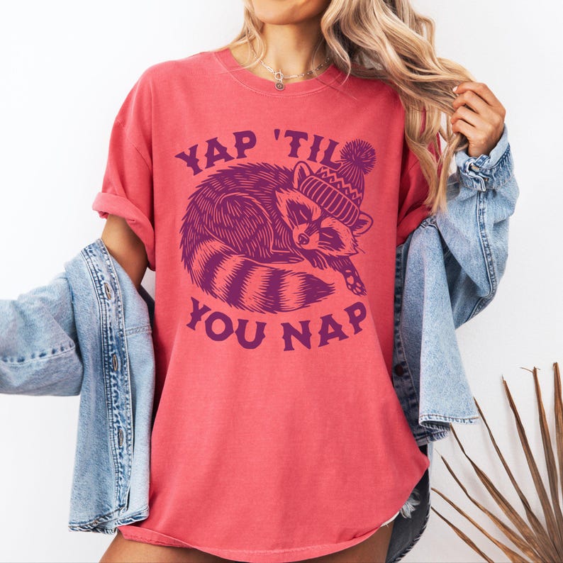 May include: A red t-shirt with a purple graphic of a raccoon wearing a hat and the text "YAP 'TIL YOU NAP".