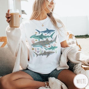 May include: A white ceramic mug with a black handle and the text "But First, Coffee" in a handwritten style. The mug is on a white surface. The mug is approximately 4 inches tall.