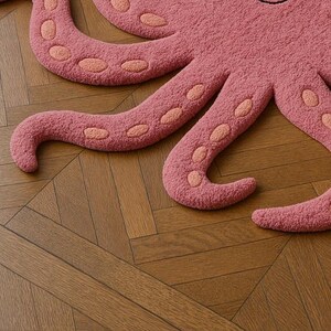 May include: A tufted rug shaped like an octopus, featuring a textured dusty pink surface with lighter peach-colored oval suction cup details along the underside of each curved tentacle, creating a distinct marine-inspired floor covering.