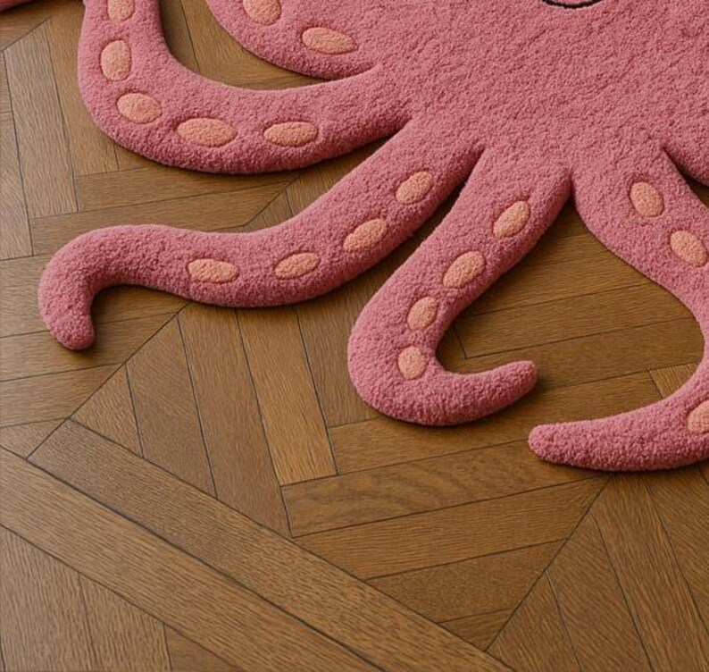 May include: A tufted rug shaped like an octopus, featuring a textured dusty pink surface with lighter peach-colored oval suction cup details along the underside of each curved tentacle, creating a distinct marine-inspired floor covering.