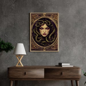 May include: A framed illustration of a woman with snakes for hair. The woman has dark hair and green eyes. The frame is gold with ornate details.