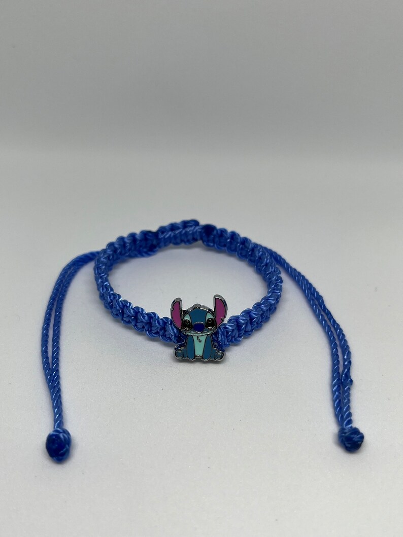 May include: Blue braided friendship bracelet with a blue Stitch character charm. The bracelet has two long ties.