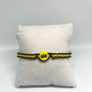 May include: A black and yellow braided bracelet with a yellow Batman logo charm.