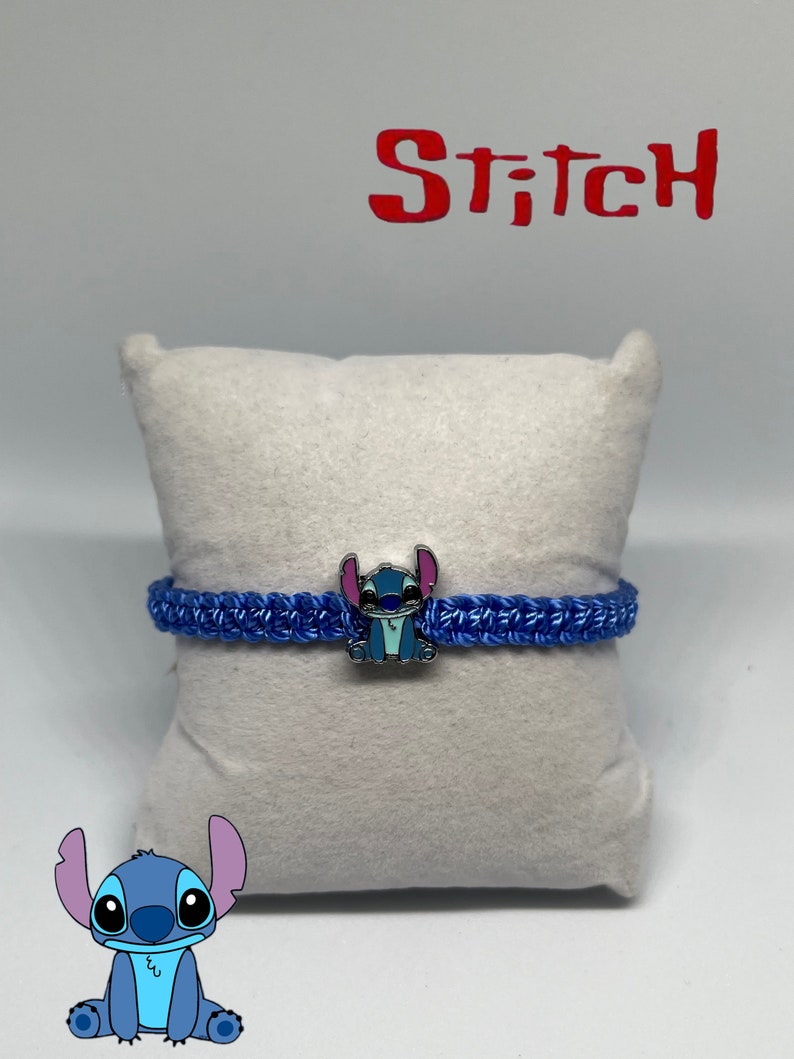 May include: Blue and white Stitch character charm bracelet with blue braided cord. The bracelet is displayed on a white cushion with the word "Stitch" in red letters above it.