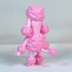 K&ouml;nnte beinhalten: Eine rosafarbene Pudelfigur mit einem flauschigen, lockigen Fell. Der Pudel steht auf einer wei&szlig;en Oberfl&auml;che.