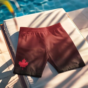 Könnte beinhalten: Rote und schwarze Badehose mit kanadischem Flaggenmuster. Die Hose liegt auf einem weißen Liegestuhl.
