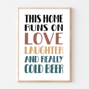 Pode incluir: Uma impressão emoldurada com o texto "This home runs on love laughter and really cold beer". O texto está em preto, marrom, amarelo e azul.