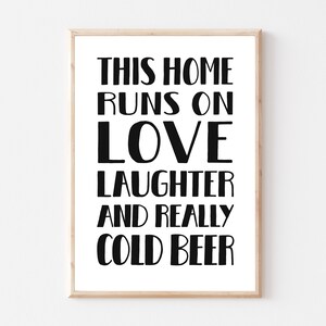 Pode incluir: Uma impressão emoldurada com texto preto em fundo branco. O texto diz "This home runs on love laughter and really cold beer."