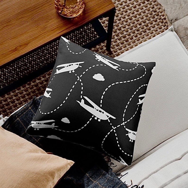 May include: Black throw pillow with a white airplane pattern. The airplanes are flying along dotted lines with clouds in the background.