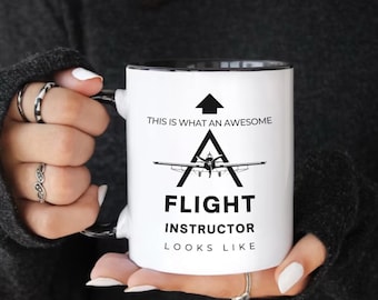 May include: White ceramic mug with a black rim and handle. The mug has a black graphic of a plane with the text "This is what an awesome flight instructor looks like."